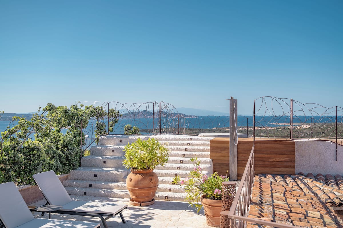 A rooftop terrace with steps leading to a wooden deck, potted plants, and a view of the sea.
