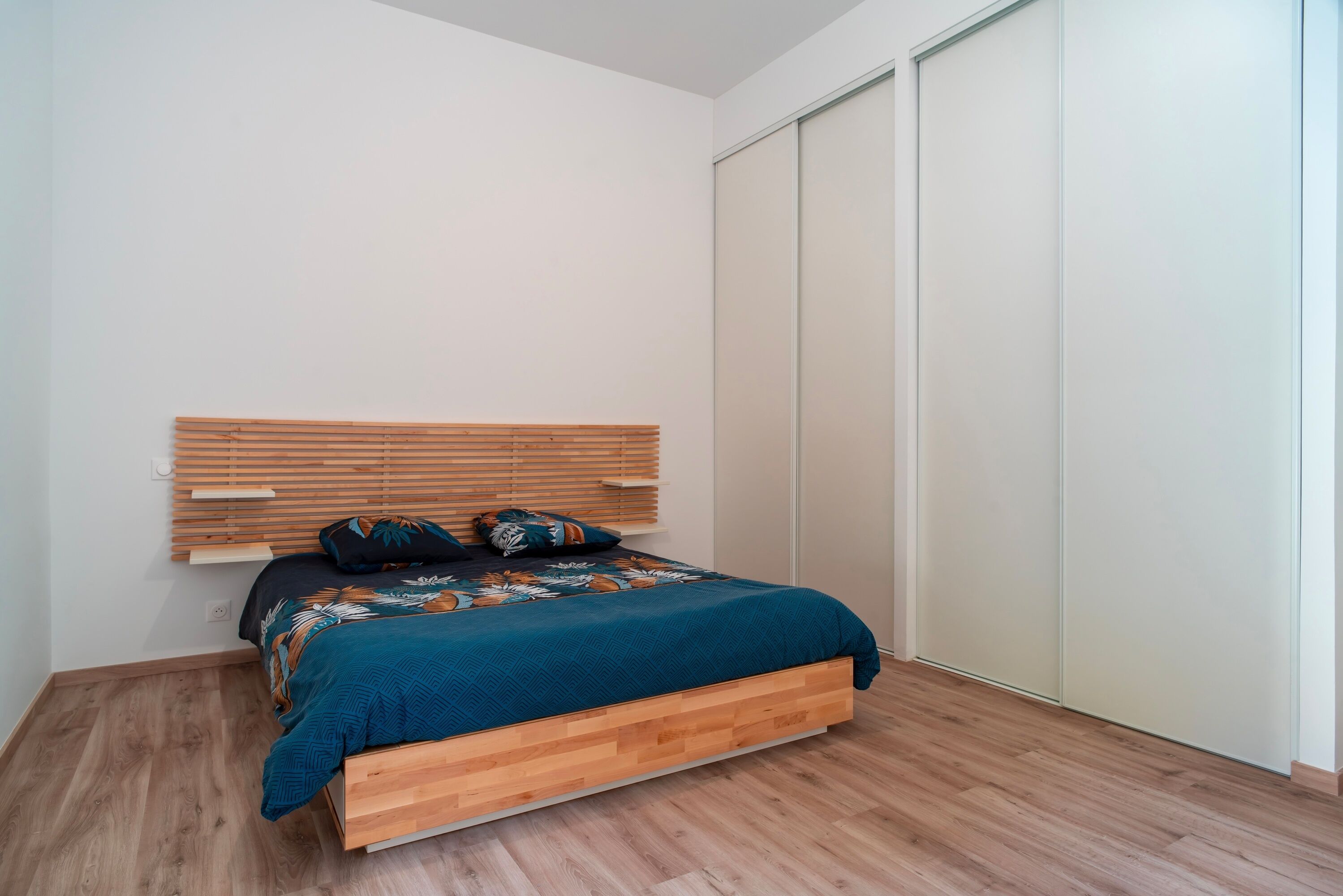 Une chambre à coucher avec un cadre de lit en bois, une couvre-lit de couleur turquoise et un plancher en bois.