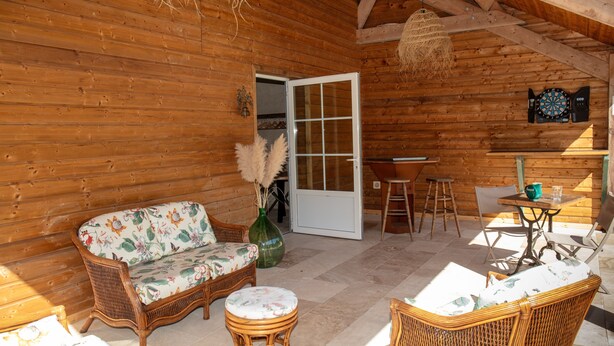 A wooden cabin interior with a sofa, chairs, a table, and a dartboard.