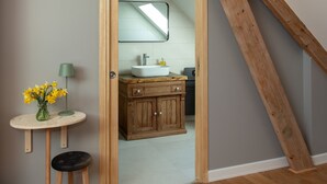 A bathroom with a wooden vanity, a sink, and a mirror. There is a small table with a vase of flowers and a lamp.