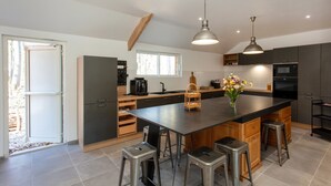 A modern kitchen with a central island, bar stools, a coffee machine, and a vase of flowers.