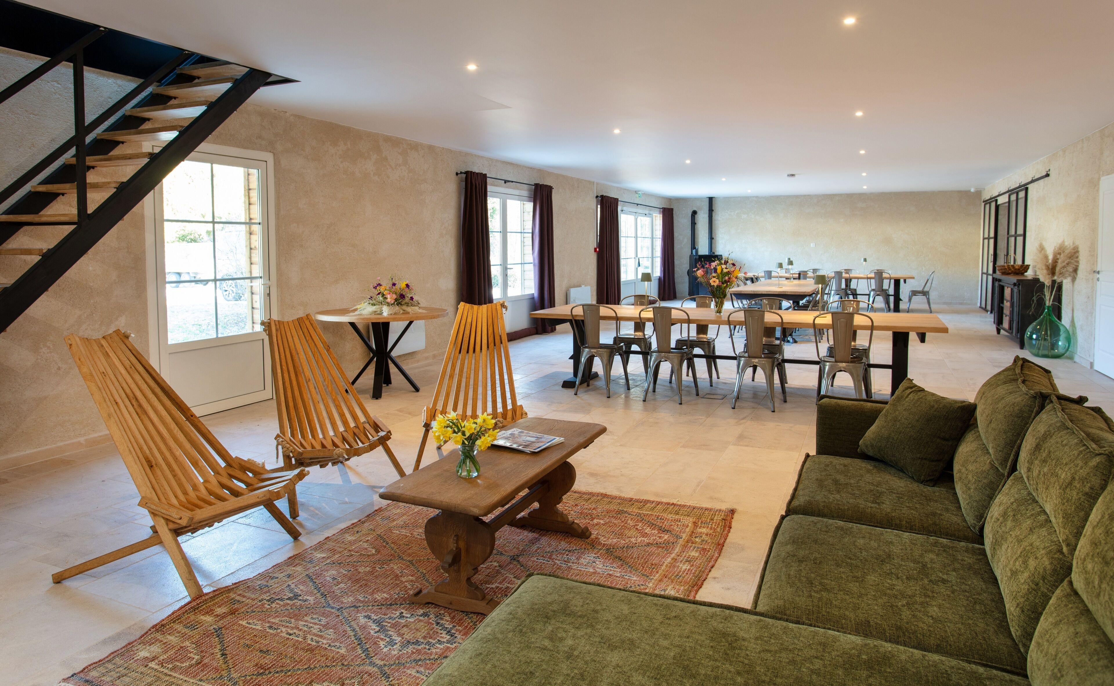 A spacious living area with a high ceiling, a staircase, a dining table with chairs, and a green sofa.