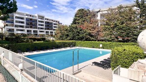 Ein Swimmingpool mit weißem Zaun, Liegestühlen und Blick auf Wohnhäuser.