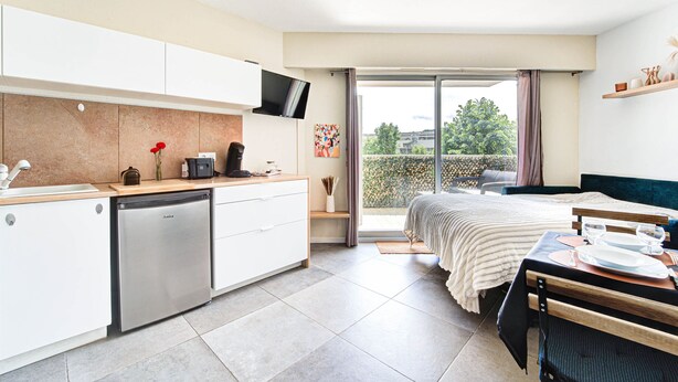 Eine moderne Küche mit Geschirrspüler, eine Essecke mit Tisch für zwei Personen und eine große Schiebeglastür, die auf einen Balkon führt.