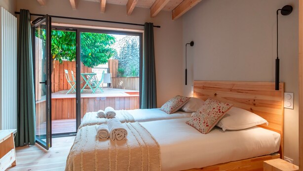 Una cama doble con cabecera de madera, una mesita de noche pequeña y vistas a una terraza exterior con mesa y sillas.