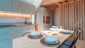 Una cocina moderna con armarios grises, una mesa de comedor de madera dispuesta con platos y vasos, y una estructura de techo de madera.