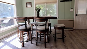 A dining area with a wooden table and six chairs, a window with blinds, a small plant on the table, and a door with a coat rack. - Good Decision on the Mo- Cascade, MT (Cascade)