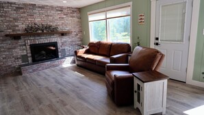 A living room with a brick fireplace, a brown leather sofa, and a white cabinet. - Good Decision on the Mo- Cascade, MT (Cascade)
