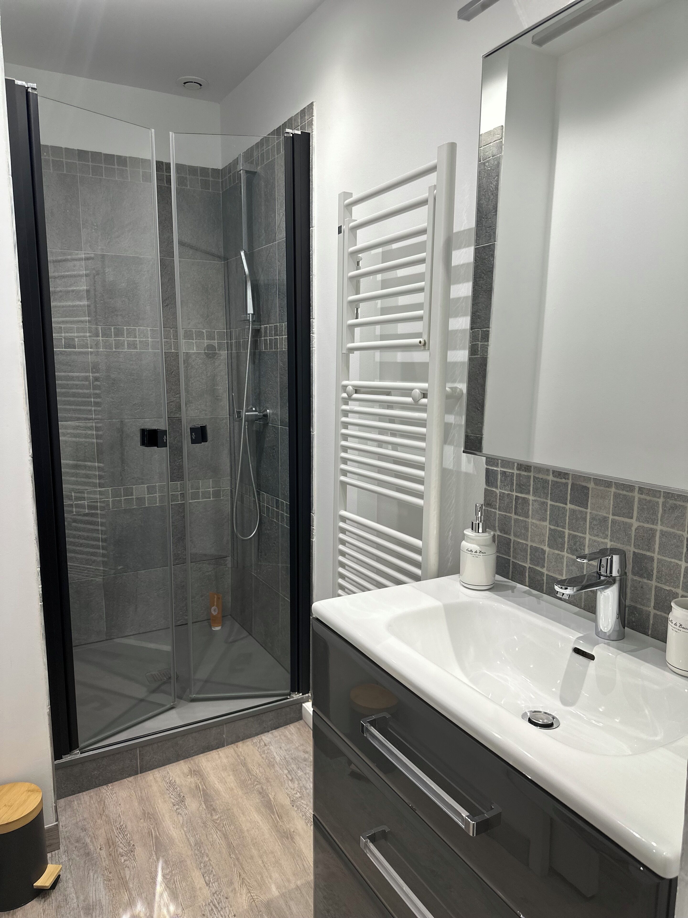 Een moderne badkamer met een douchecabine van glas, een witte wastafel met een enkele kraan, en een spiegel boven de wastafel.