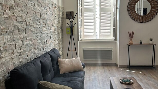 Ein modernes Wohnzimmer mit einer Steinwand, einem dunklen Sofa, einem Holztisch und einem großen Fenster mit Fensterläden.