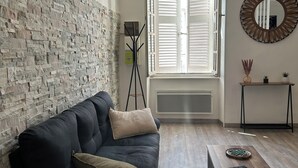 A modern living room with a stone wall, a dark sofa, a wooden coffee table, and a large window with shutters. - The Charm of Anduze (Anduze)