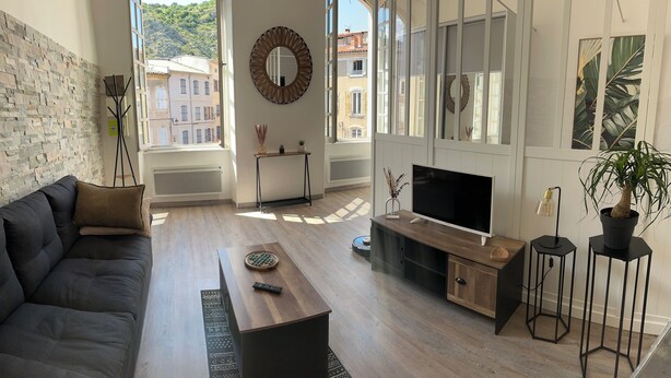 A modern living room with a sofa, TV, wooden coffee table, and a view of buildings through large windows. - The Charm of Anduze (Anduze)