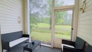A porch with wicker furniture, a glass door, and a view of a grassy area.