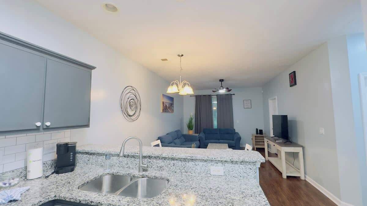 A modern kitchen with granite countertops, a double sink, and a built-in oven. There is a seating area with a blue sofa and a small table.