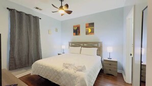 A bedroom with a bed, a ceiling fan, two bedside tables with lamps, a door, and a curtain.