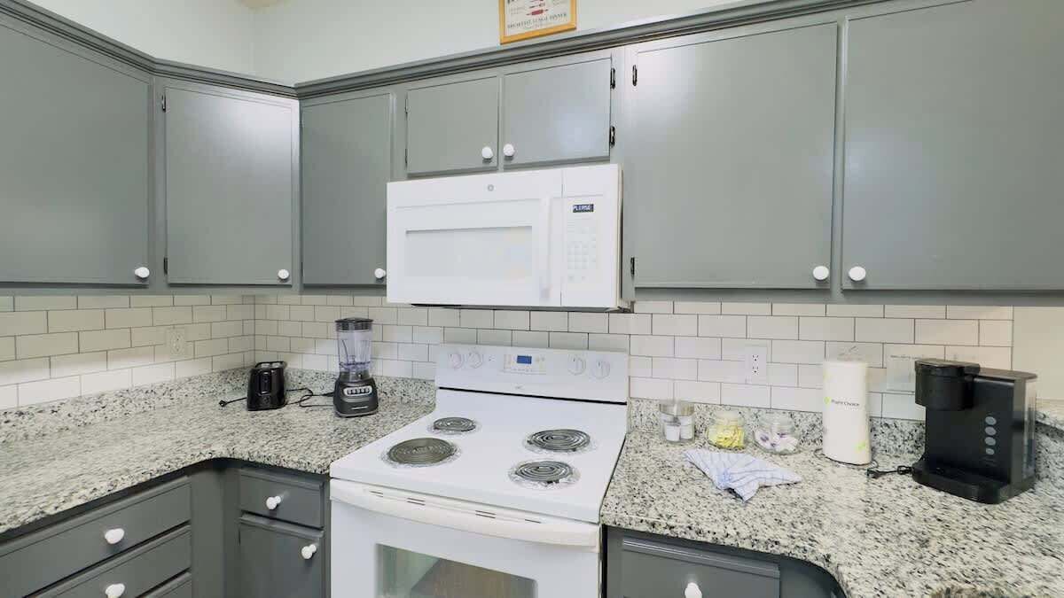 A kitchen with grey cabinets, a white stove, and a microwave. There is a coffee maker and a blender on the counter.