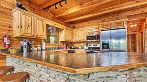 A spacious kitchen with wooden cabinets, a large island with stools, a stone accent wall, and stainless steel appliances.