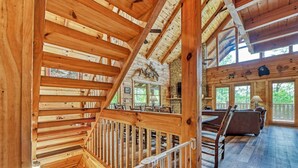 A wooden interior with a staircase, a dining area with a table and chairs, and a stone fireplace.