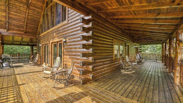 A log cabin with a covered porch, wooden furniture, and a view of the outdoors.