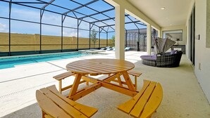 Ein überdachter Außenbereich mit Pool, einem Holztisch, Liegestühlen und einer Rattan-Couch.