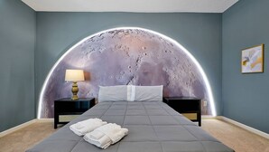 Ein Schlafzimmer mit gewölbter Decke, einem Bett mit grauer Bettdecke, zwei Nachttischen mit Lampen und einem Wandbild.