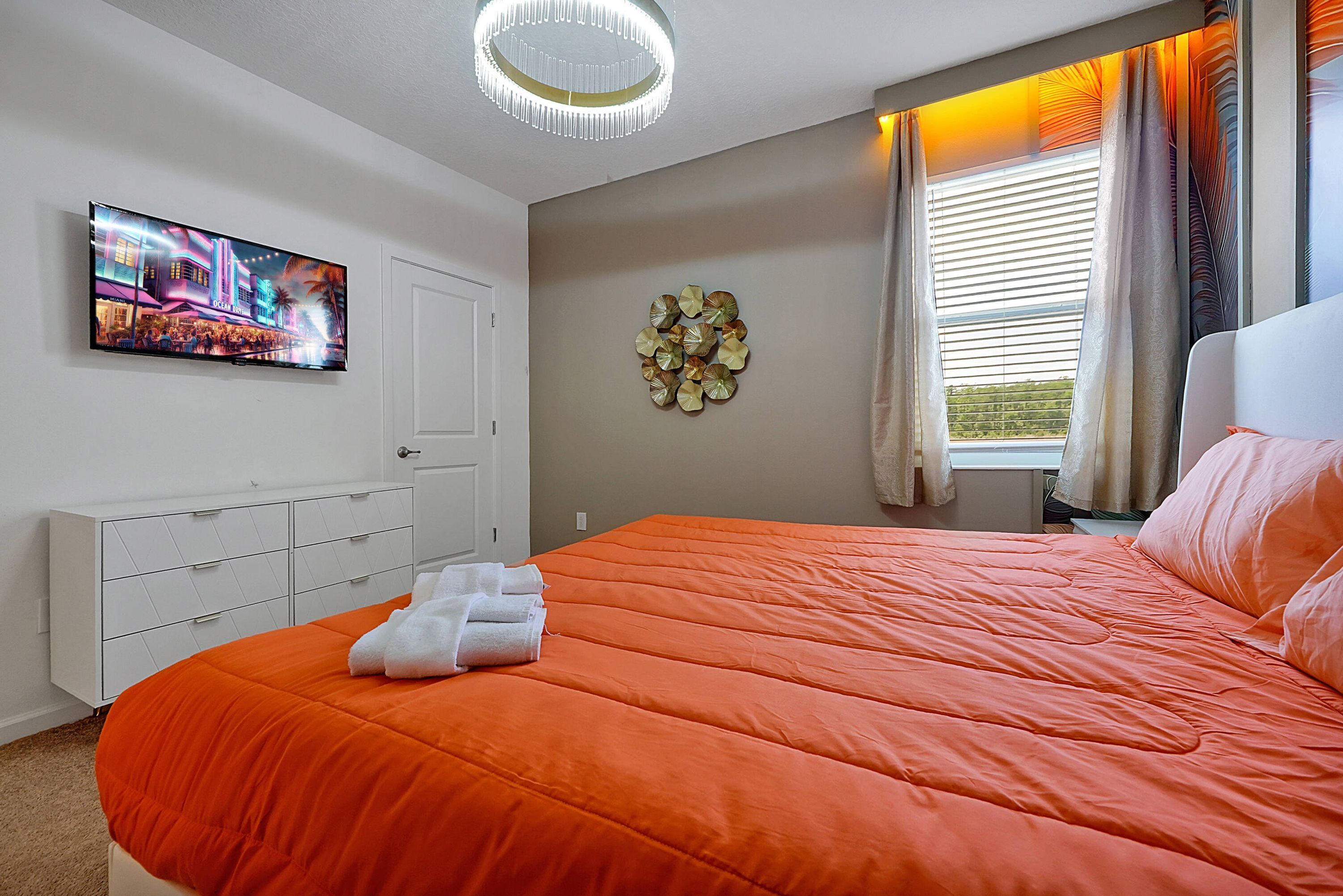 Une chambre d’hôtel avec un grand lit, un téléviseur à écran plat fixé au mur, une commode blanche et une fenêtre avec des rideaux.