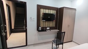 A room with a wooden wardrobe, a small table, a chair, a microwave, and a power outlet. - Hotel Shri Vishwanath (Varanasi)