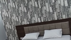 A modern bedroom with a large bed, a headboard, and a patterned wall. - Hotel Shri Vishwanath (Varanasi)