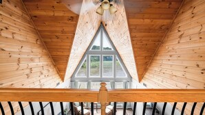 A wooden interior with a sloped ceiling, a central window, and a view of greenery outside. - Spacious 4BR Cabin in Doniphan – Perfect for Family Getaways (Doniphan)