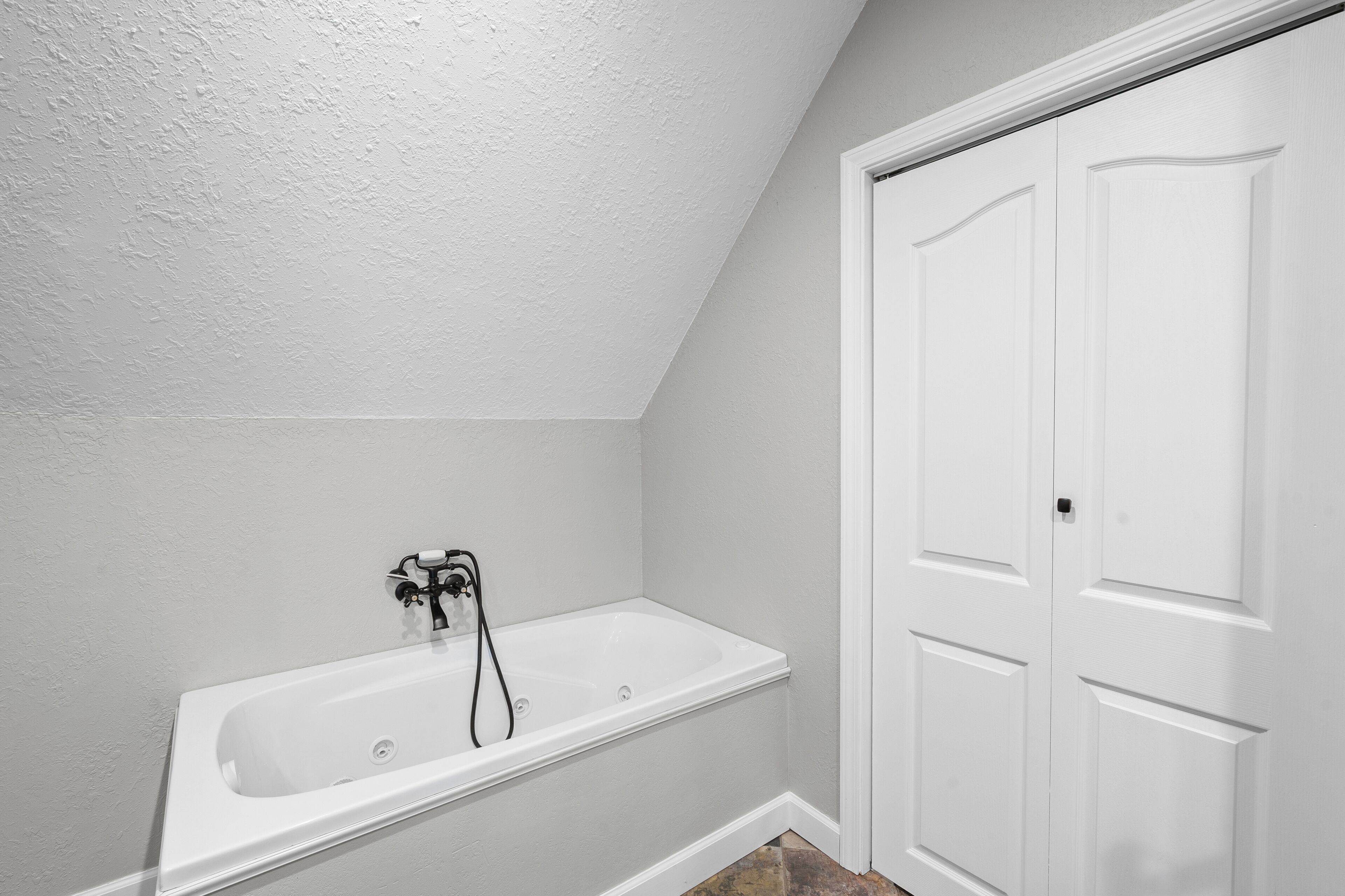 Une salle de bain avec une baignoire blanche, une porte et un plafond à texture.