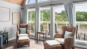 A room with wicker chairs, a small table, and large windows overlooking a river. - Spacious 4BR Cabin in Doniphan – Perfect for Family Getaways (Doniphan)