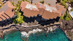 Vue aérienne d’un hôtel situé sur la côte, composé de plusieurs bâtiments, avec une eau turquoise cristalline et une côte rocheuse.