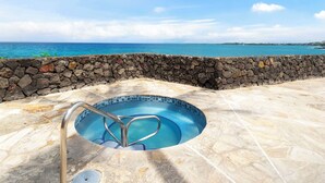 Une piscine bordée d’un mur en pierre et dotée d’un escalier en métal, entourée d’une terrasse en pierre, et offrant une vue sur l’océan.