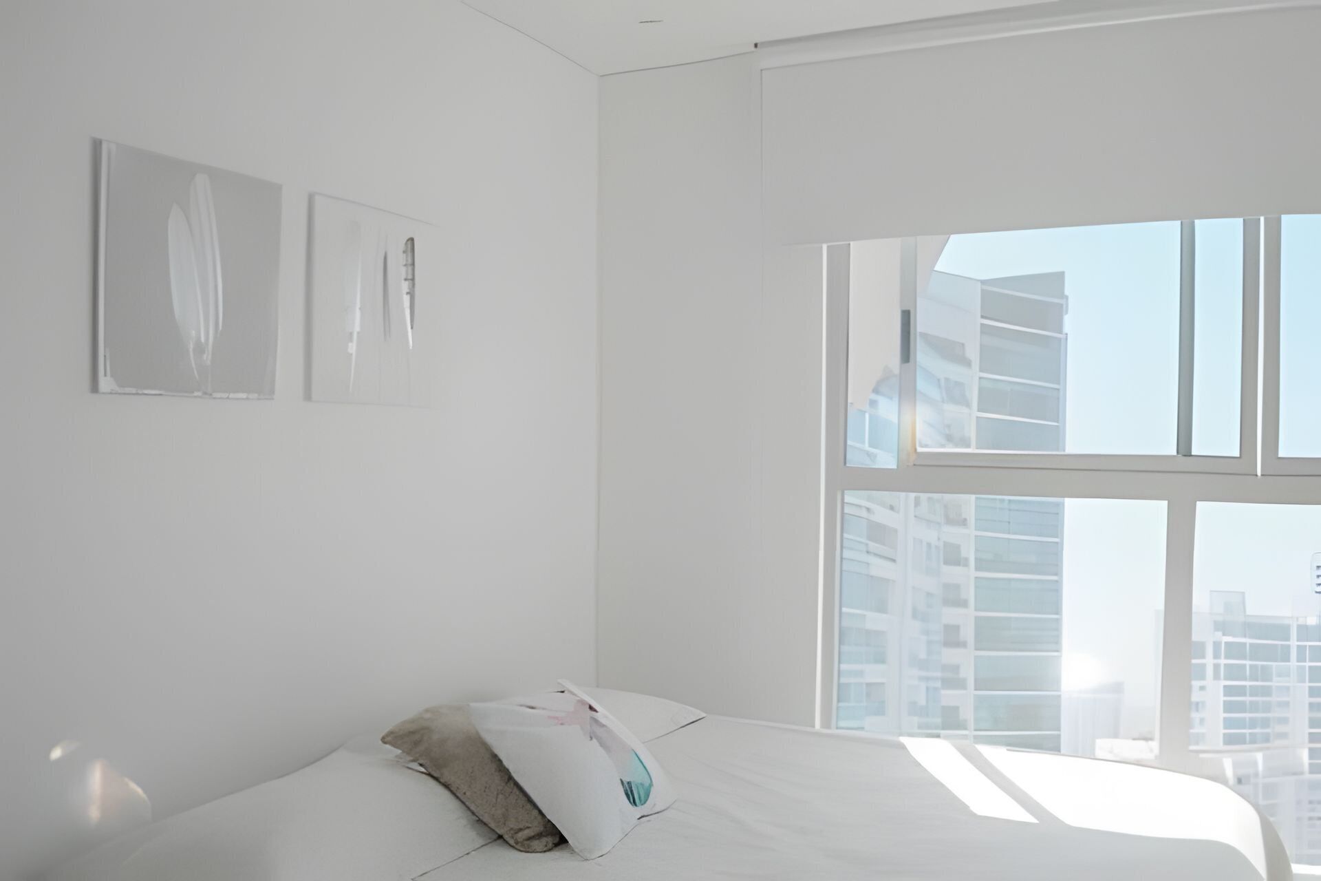 A minimalist bedroom with a large window, white walls, and a bed with a pillow.
