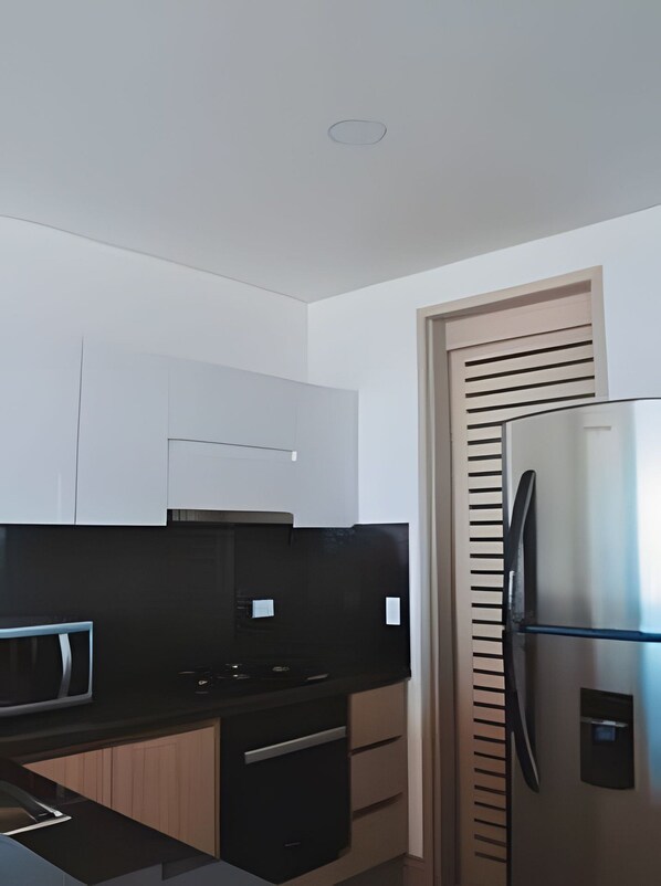 A modern kitchen with white cabinets, a black countertop, and a stainless steel refrigerator.