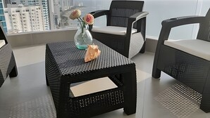 A modern balcony with wicker furniture, a glass vase with flowers, and a view of a cityscape. - Murano Elite Bocagrande (Cartagena)