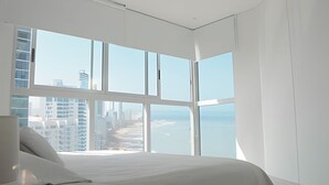 A modern bedroom with a large window offering a view of a cityscape and the ocean. - Murano Elite Bocagrande (Cartagena)