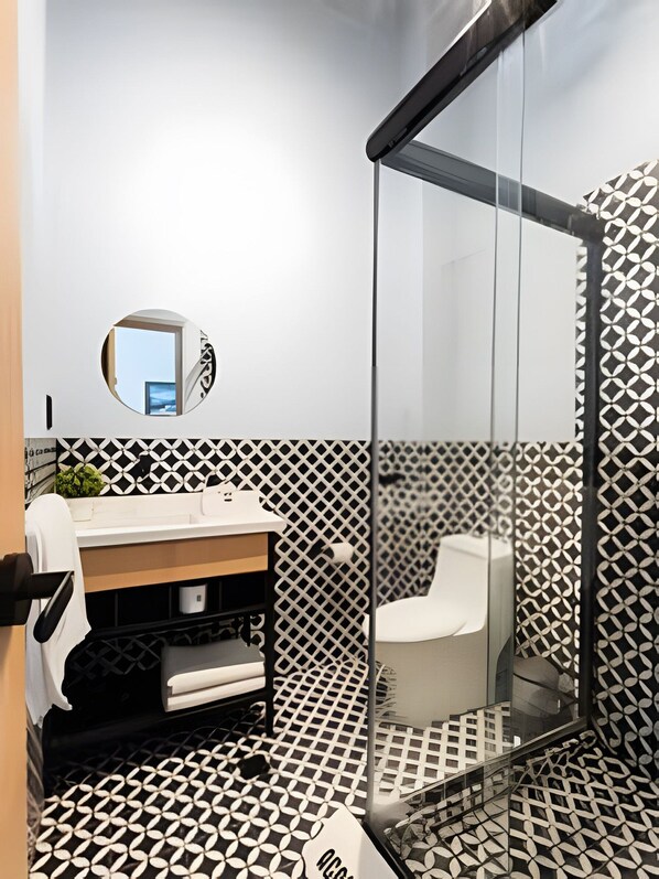 Un baño moderno con ducha envuelta en vidrio, un espejo redondo y un piso con diseño blanco y negro.