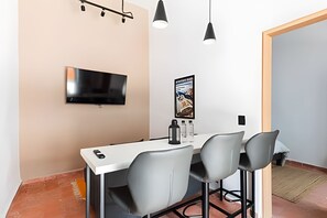 Ein zeitgemäßer Essbereich mit einem weißen Tisch, drei grauen Stühlen, einem schwarzen Fernseher und einem Poster an der Wand.