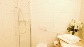 Un baño con ducha de vidrio, inodoro, lavamanos con toalla y una pequeña planta en maceta.