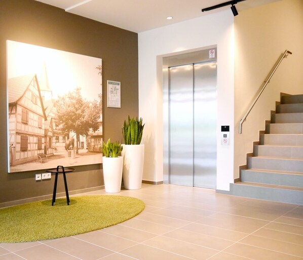 Eine moderne Lobby mit einem großen historischen Foto, einem grünen Teppich, einem Aufzug und einer Treppe.