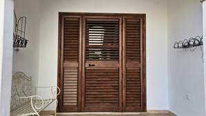 Een houten deur met horizontale latten, een metalen bank en een wandrek met haken.