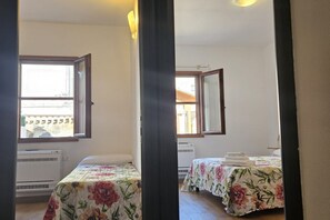 Una stanza con due letti, ognuno con una coperta a fiori, una finestra e un condizionatore d'aria.