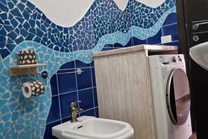 Un bagno con parete in mosaico, un lavandino, un porta carta igienica e una lavatrice.