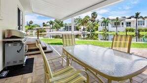 A covered patio with a grill, a glass table, and striped chairs.