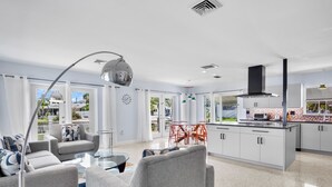 A modern living room with grey sofas, a glass coffee table, and a dining area with red chairs.