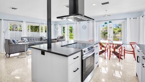 A modern kitchen with a central island, built-in oven, and a dining area with red chairs.