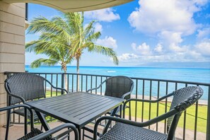 A balcony with a table and chairs overlooking a beach with a palm tree and ocean view.