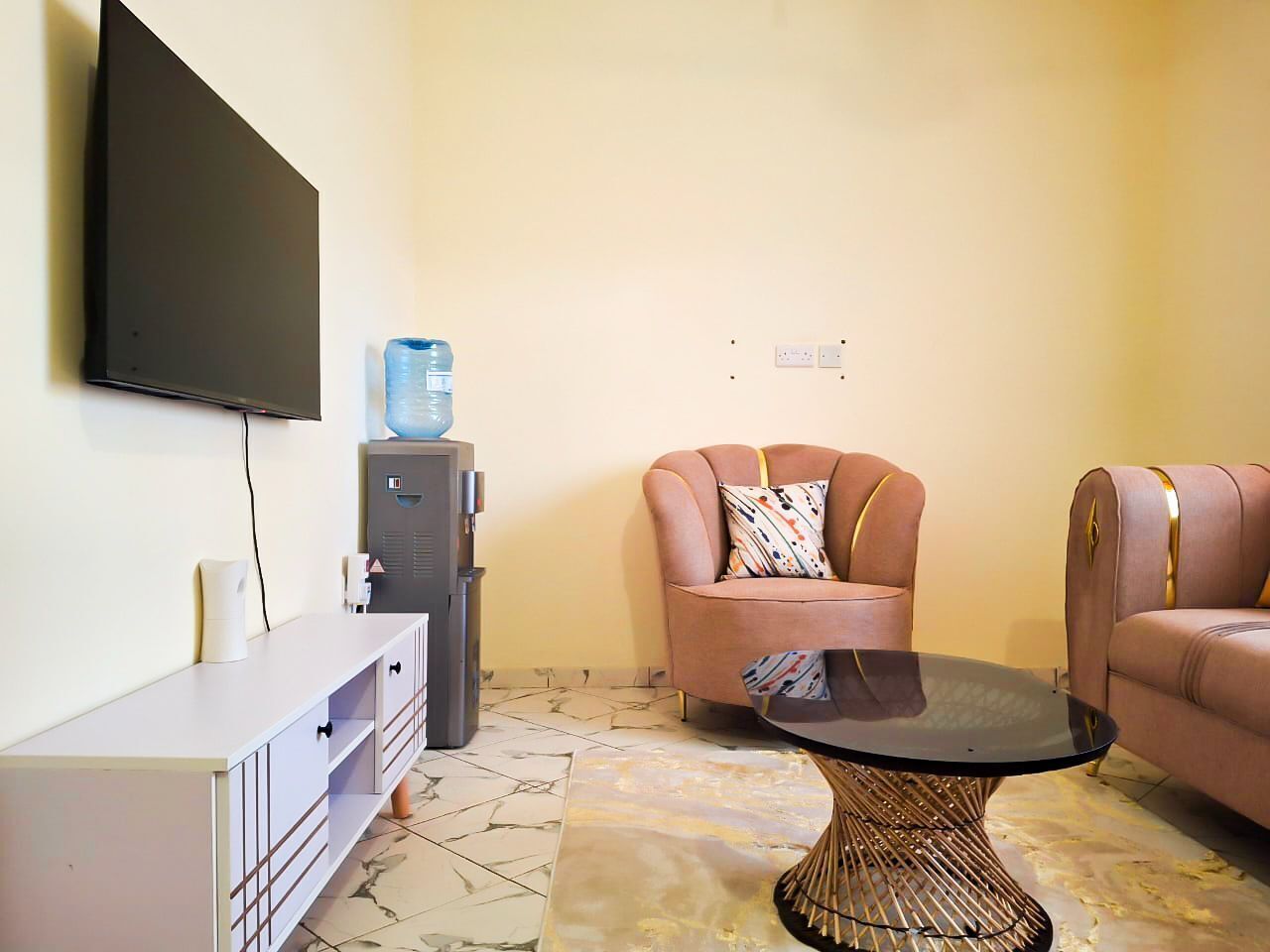 Un salon équipé d’un téléviseur à écran plat fixé au mur, d’un distributeur d’eau, d’un canapé, d’une table basse et d’un meuble de rangement.