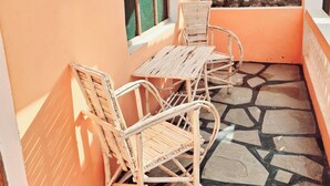 A small, enclosed balcony with a table and two wicker chairs, a window with a mesh screen, and a stone wall with climbing plants. - Zai Homes Watamu (Watamu)